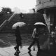 Passanten mit Regenschirmen hasten durch eine städtische Umgebung