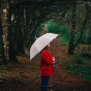 Frau steht mit einem aufgespanntem Regenschirm im Wald